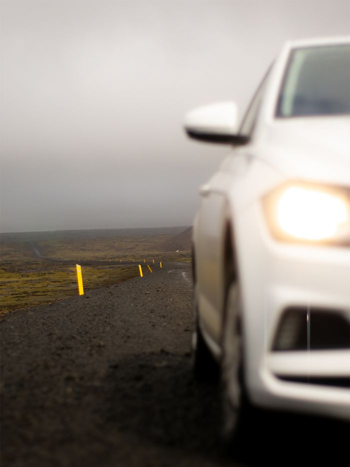 A white car with headlights on driving on a foggy remote road in Iceland, showcasing travel adventure.
